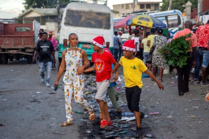 Une femme marche avec ses garçons dans une rue tout en portant des bonnets de Noël à Port-au-Prince, en Haïti, jeudi 24 décembre 2021. © Dieu Nalio Chery/AP