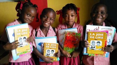 Quatre jeunes écoliers haïtiens tenant des ouvrages scolaires entre les mains.