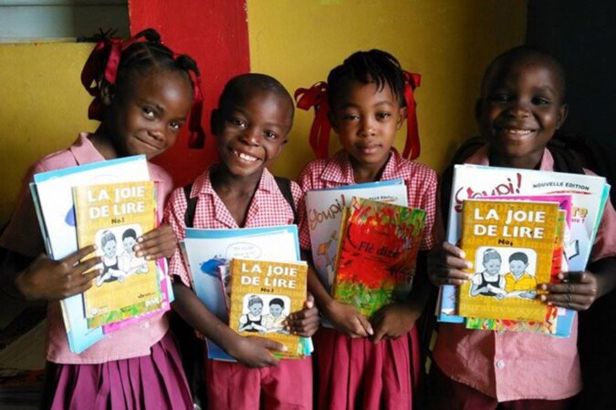 Quatre jeunes écoliers haïtiens tenant des ouvrages scolaires entre les mains.