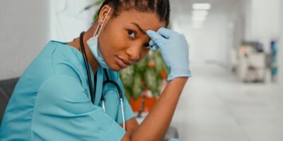 Photo d'une jeune médecin assise dans un couloir d'hôpital, une main posée contre la tête.