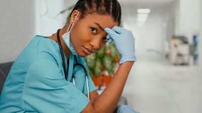 Photo d'une jeune médecin assise dans un couloir d'hôpital, une main posée contre la tête.