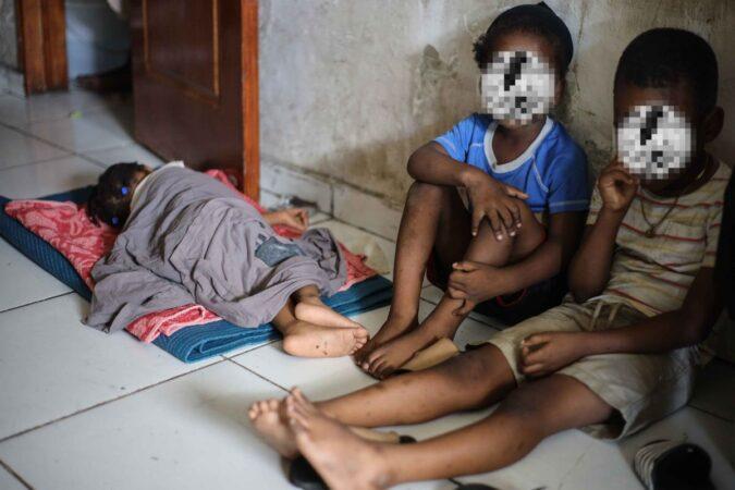Au camp de l’OPC, deux petits garçons sont assis et une petite fille est couchée à même le sol. Avril 2025. Photo : Jean Feguens Regala pour AyiboPost