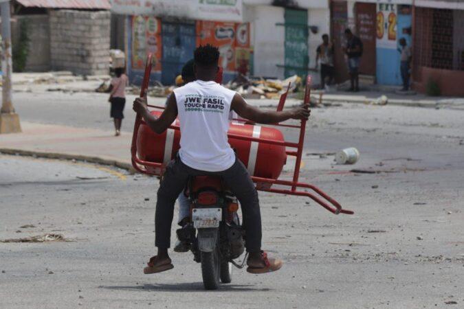 Un homme transporte une bouteille de gaz parmi les objets récupérés chez lui après le passage des gangs à Solino, le XY août 2025. Photo : Jean Feguens Regala / AyiboPost