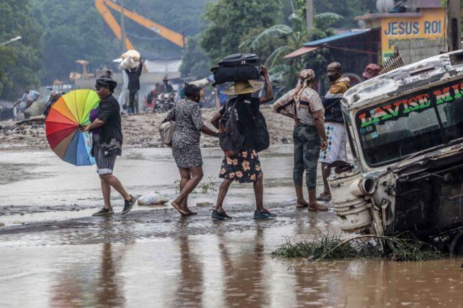 Des habitants tentent de traverser la route nationale numéro 2, inondée par la rivière, au niveau de Petit-Goâve. Vendredi 31 octobre 2025. | © Jean Feguens Regala / AyiboPost
