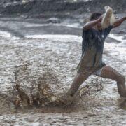 Un homme lutte contre les eaux déferlantes de la rivière La Digue pour rejoindre la douzième section de Petit-Goâve. Vendredi 31 octobre 2025. | © Jean Feguens Regala / AyiboPost