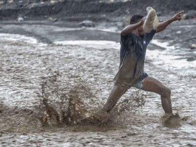 Un homme lutte contre les eaux déferlantes de la rivière La Digue pour rejoindre la douzième section de Petit-Goâve. Vendredi 31 octobre 2025. | © Jean Feguens Regala / AyiboPost