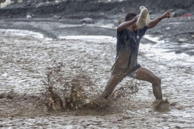 Un homme lutte contre les eaux déferlantes de la rivière La Digue pour rejoindre la douzième section de Petit-Goâve. Vendredi 31 octobre 2025. | © Jean Feguens Regala / AyiboPost