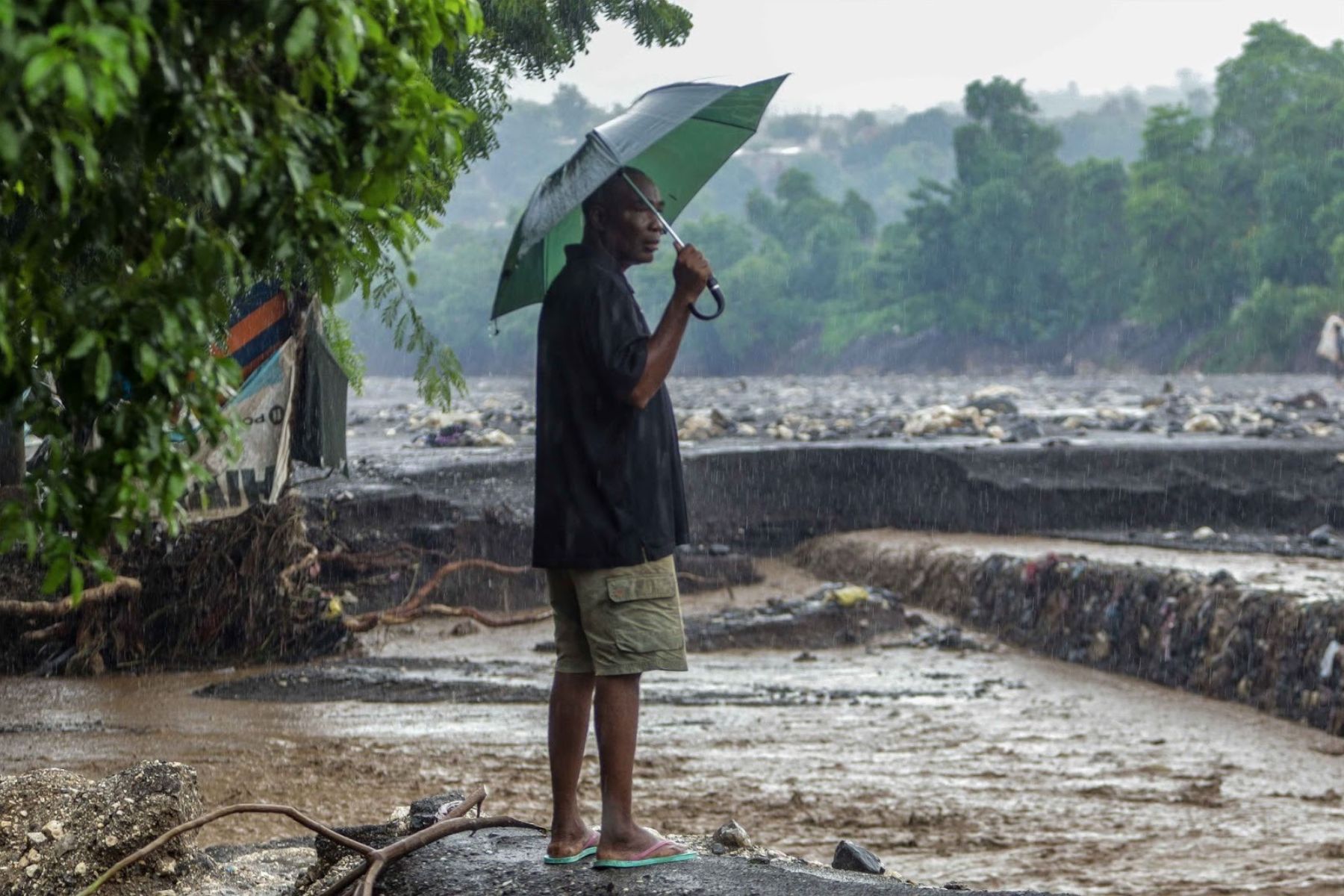Un homme observe le débordement de la rivière La Digue, qui emporte une partie de sa berge. Vendredi 31 octobre 2025. | © Jean Feguens Regala / AyiboPost